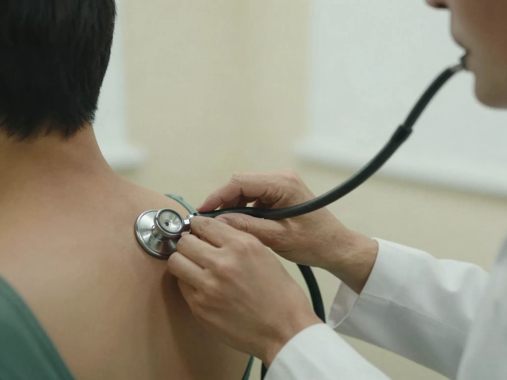 Mãos de um médico posicionando o estetoscópio nas costas de um trabalhador durante o exame ocupacional